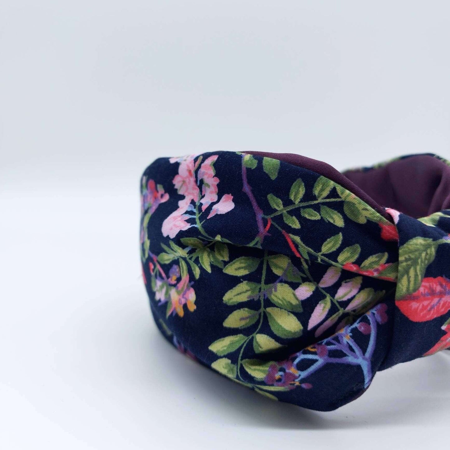 A bow-style, navy blue, red, purple and green floral fabric knot headband with purple satin lining underneath..