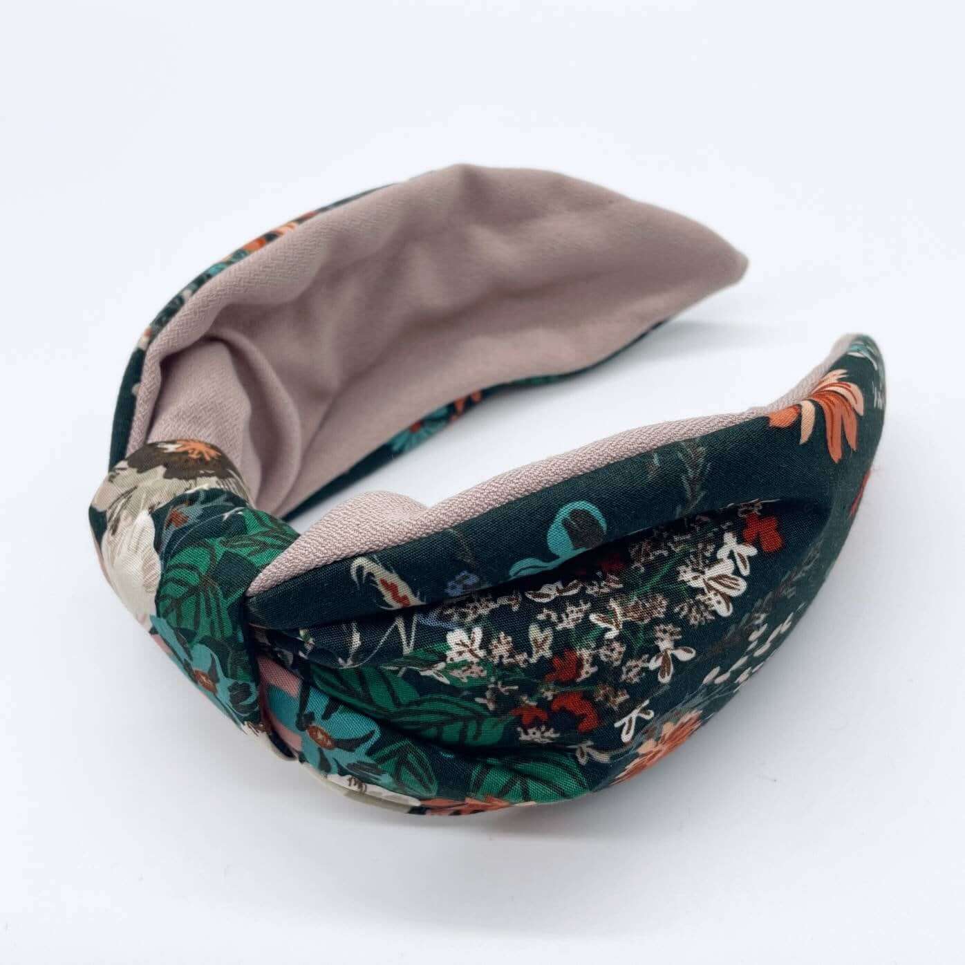 A bow-style, knot headband made from dark green fabric with orange and pink flowers and a soft pink lining underneath.