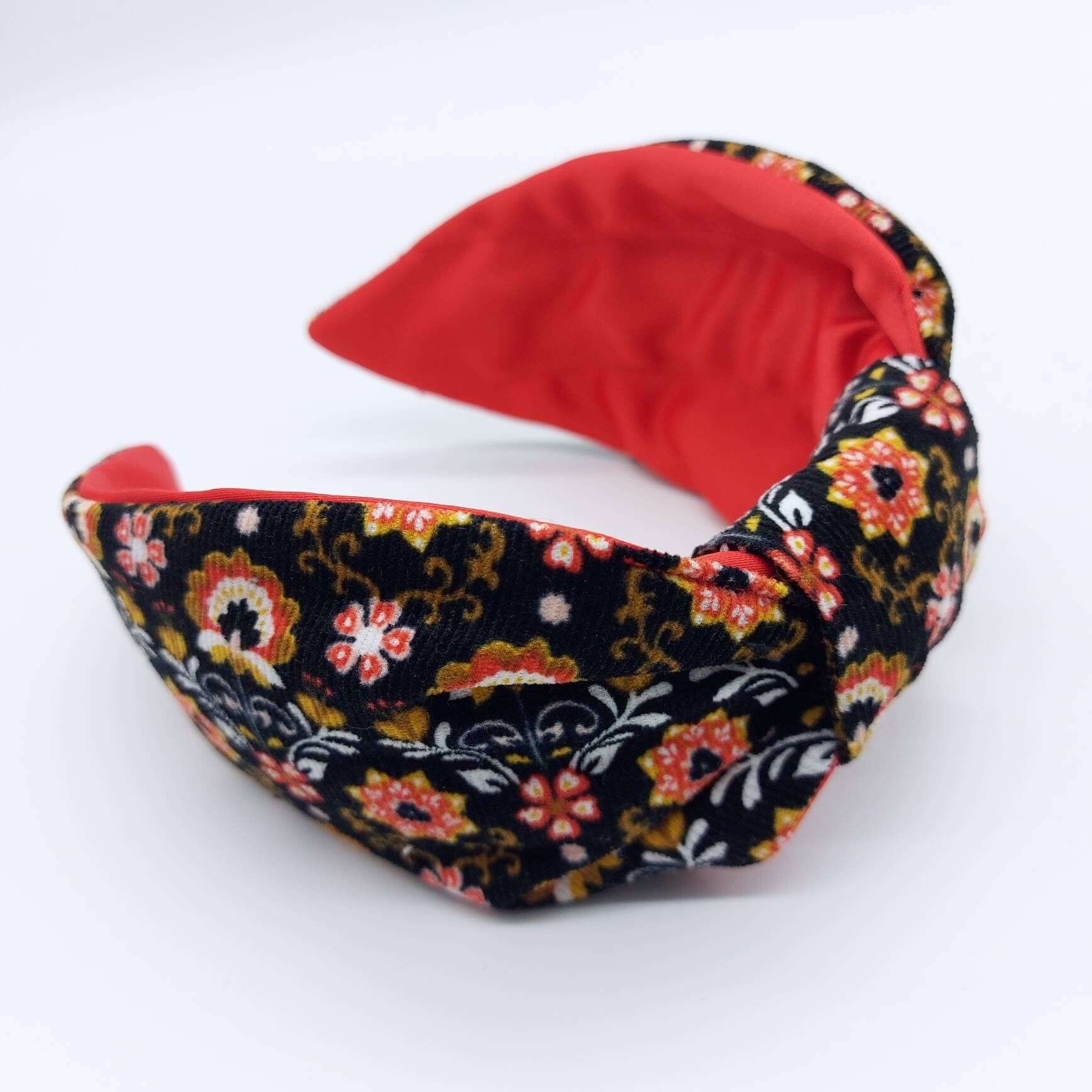 A bow-style, Scandinavian black floral-print corduroy headband with a crimson satin lining underneath.