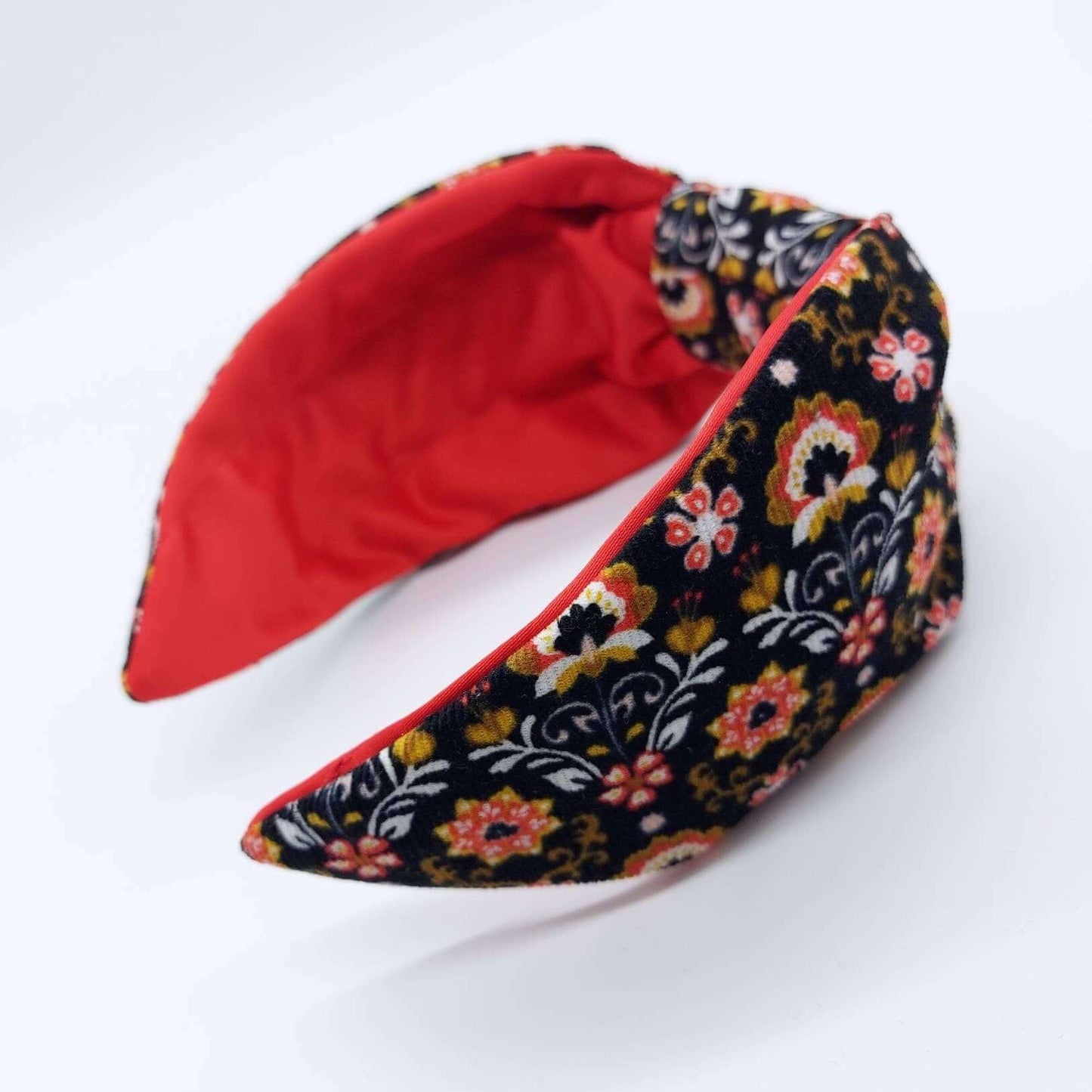 A bow-style, Scandinavian black floral-print corduroy headband with a crimson satin lining underneath.
