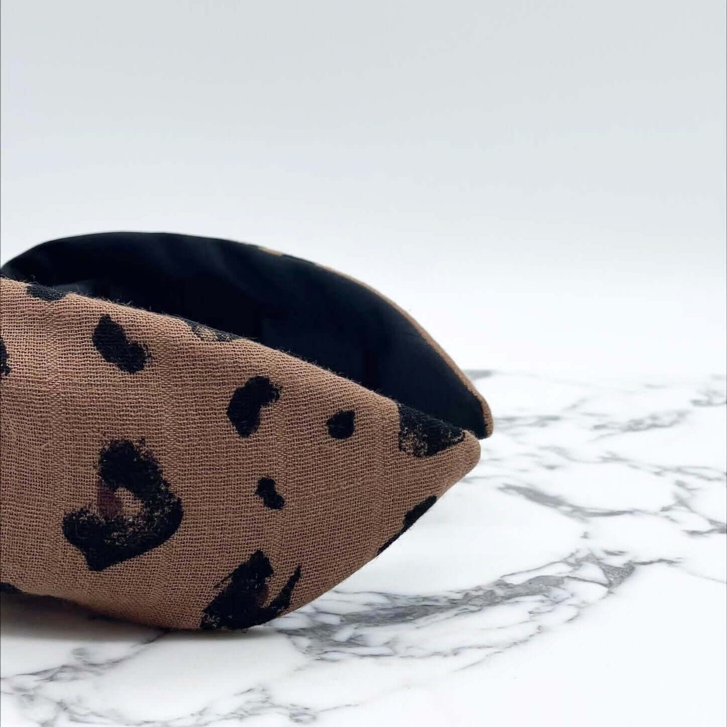 A luxury bow-style, brown and black animal print, fabric knot headband with a soft black lining underneath.