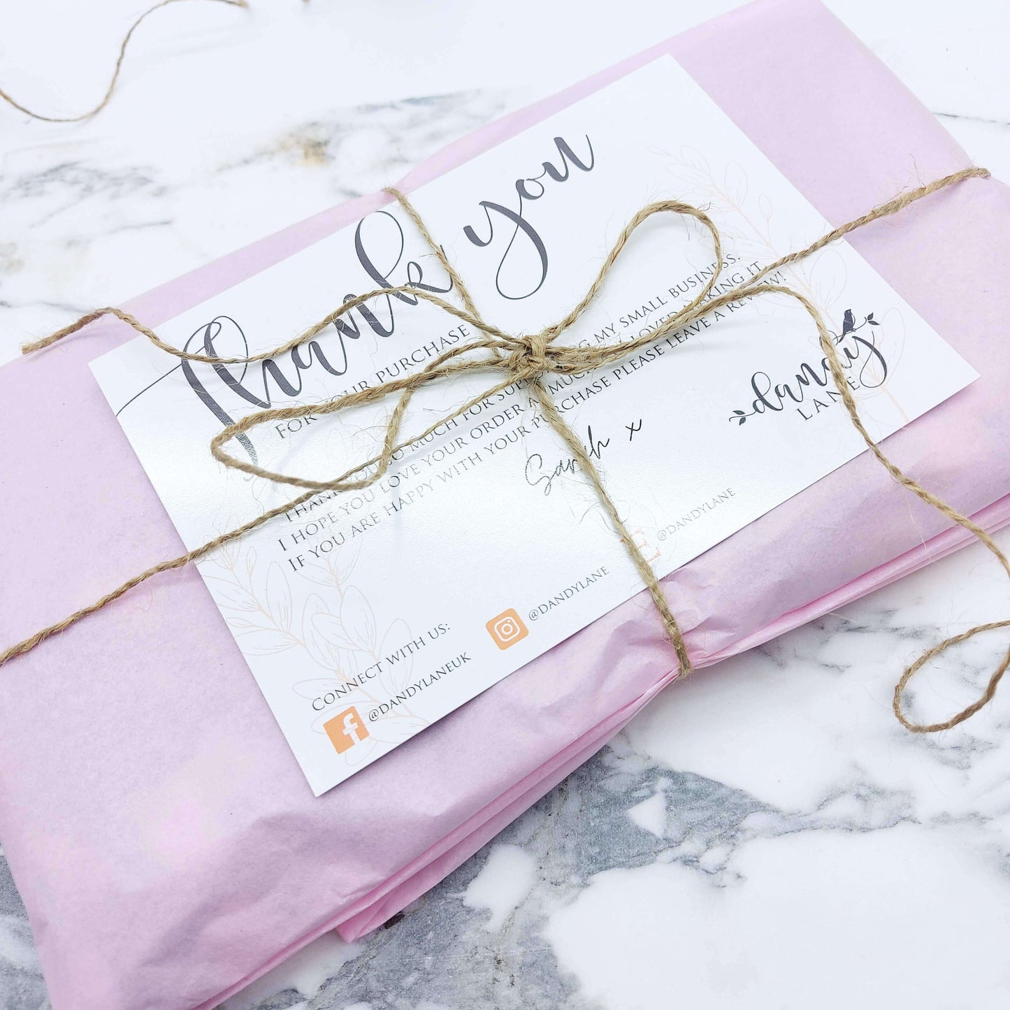 A fancy pink rectangle-shaped parcel, wrapped in pale pink tissue paper with a brown twine bow.